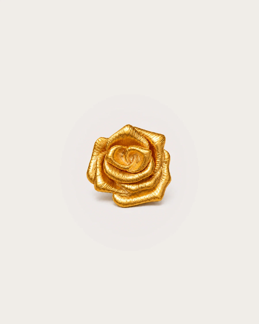 Taimi Mini Gold Camellia Brooch on a warm #F0EBE9 studio background with a natural contact shadow