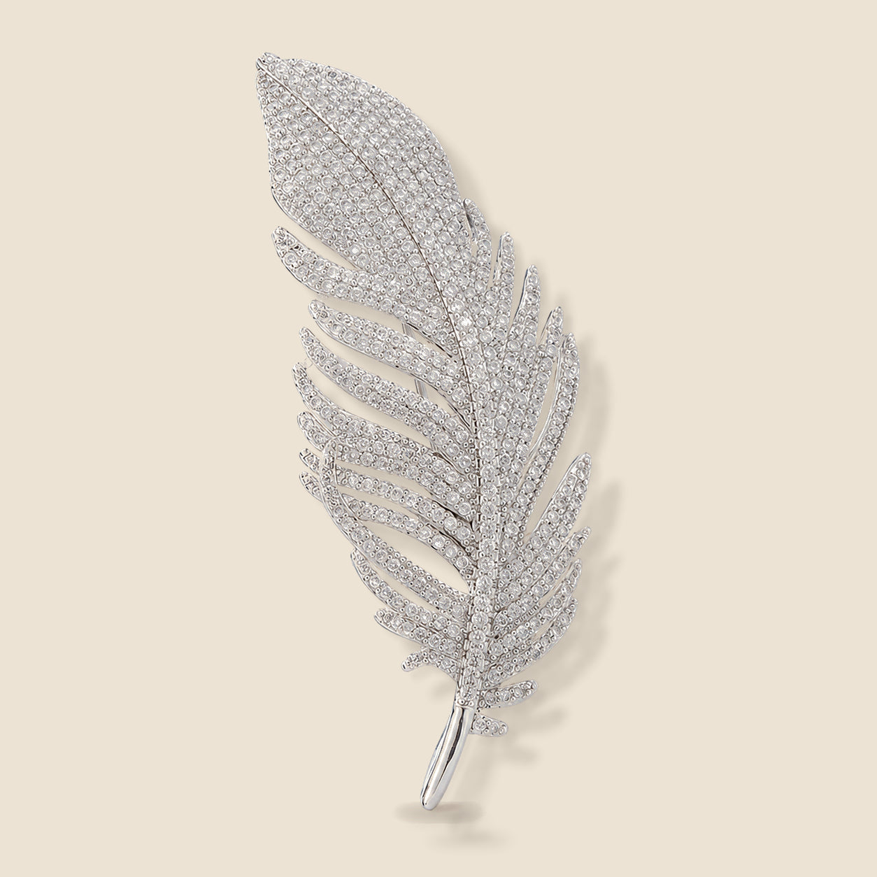 Lumi Crystal Feather Brooch in silver tone with clear crystals on a warm beige background