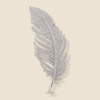 Lumi Crystal Feather Brooch in silver tone with clear crystals on a warm beige background