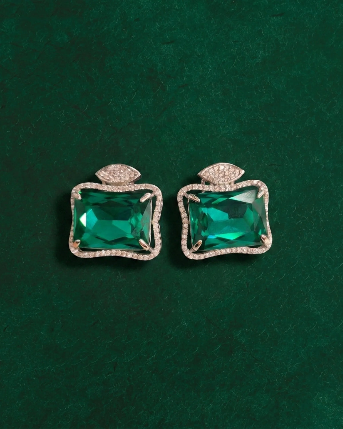 Pair of Ruutu green statement earrings on a deep green surface