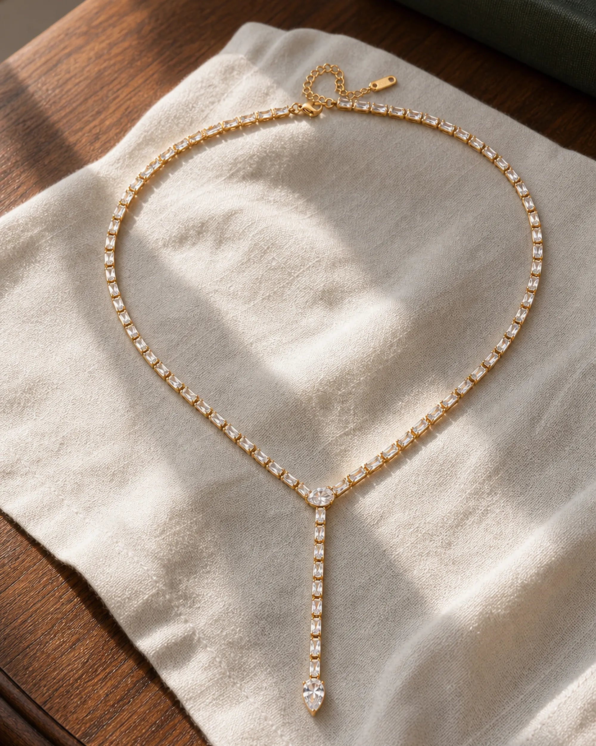 Liora Gold Crystal Y-Drop Necklace resting on ivory linen over a walnut dressing table