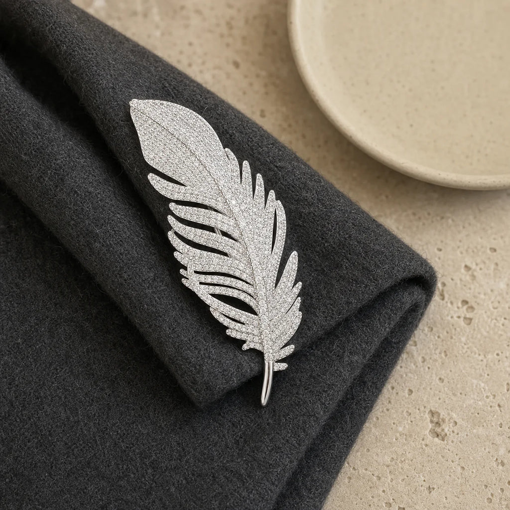 Lumi Crystal Feather Brooch displayed on folded charcoal wool and pale stone