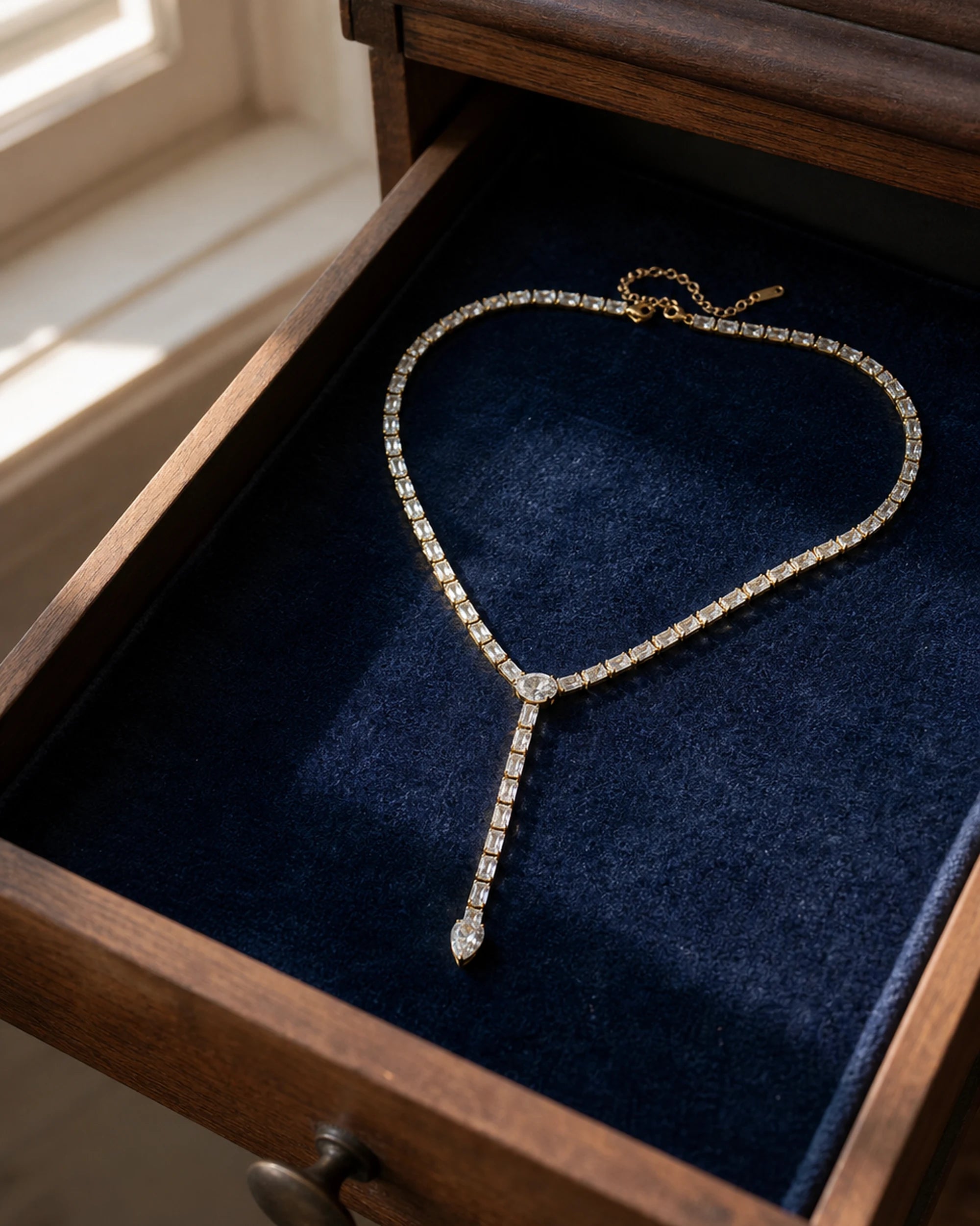Liora Gold Crystal Y-Drop Necklace arranged inside a navy velvet-lined walnut jewelry drawer