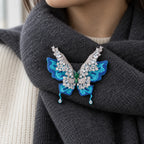 Airi butterfly brooch fastened to a charcoal wool scarf over ivory knitwear.