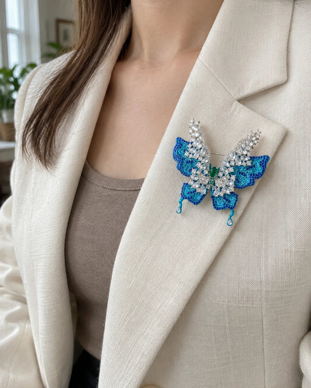 Airi blue butterfly brooch pinned within the folded lapel of an ivory blazer.