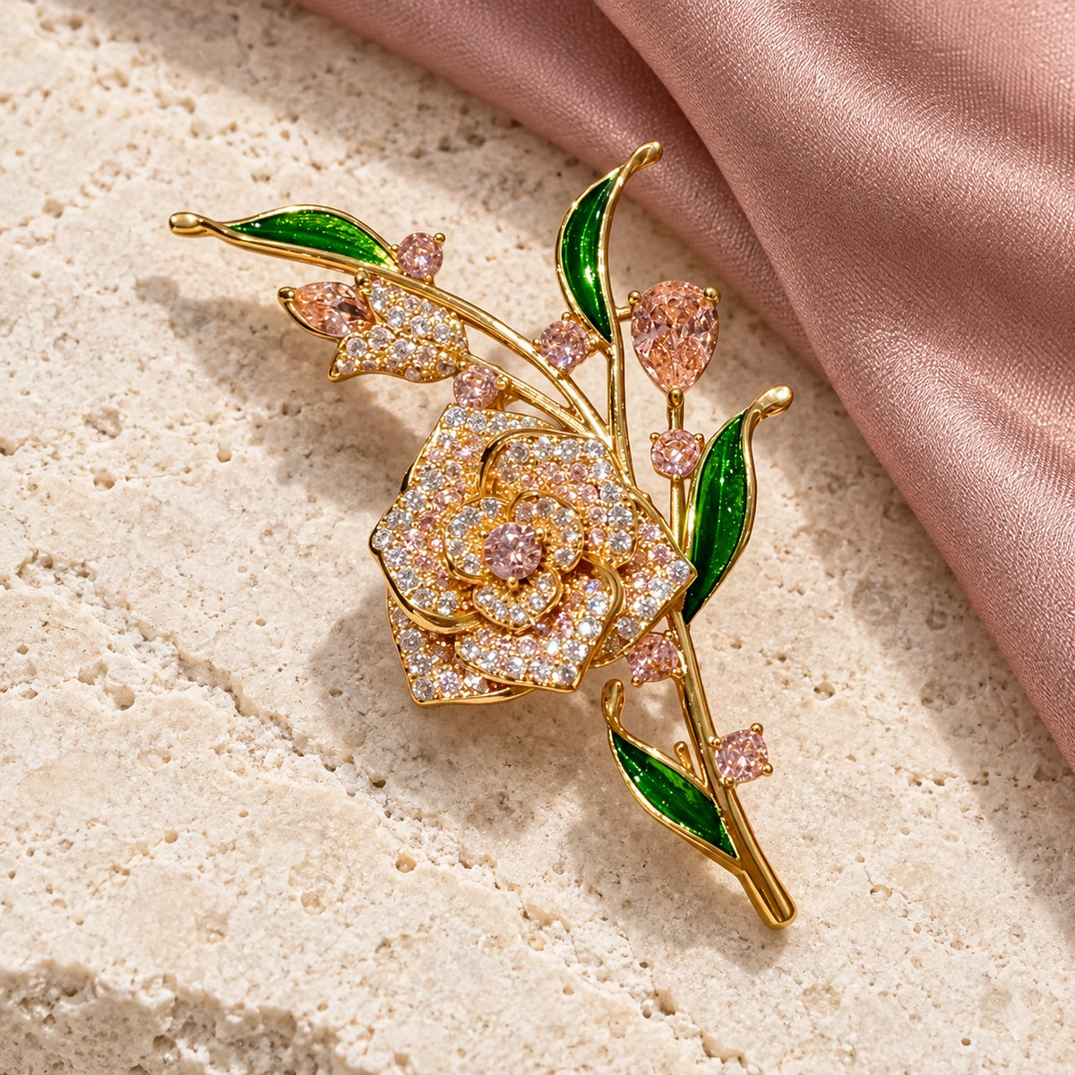 Complete Alva Pink Zircon Rose Brooch resting on pale stone beside softly folded silk.
