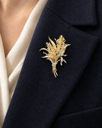 Aurea wheat sheaf brooch with curved gold-tone leaves and gathered stems on a navy coat lapel