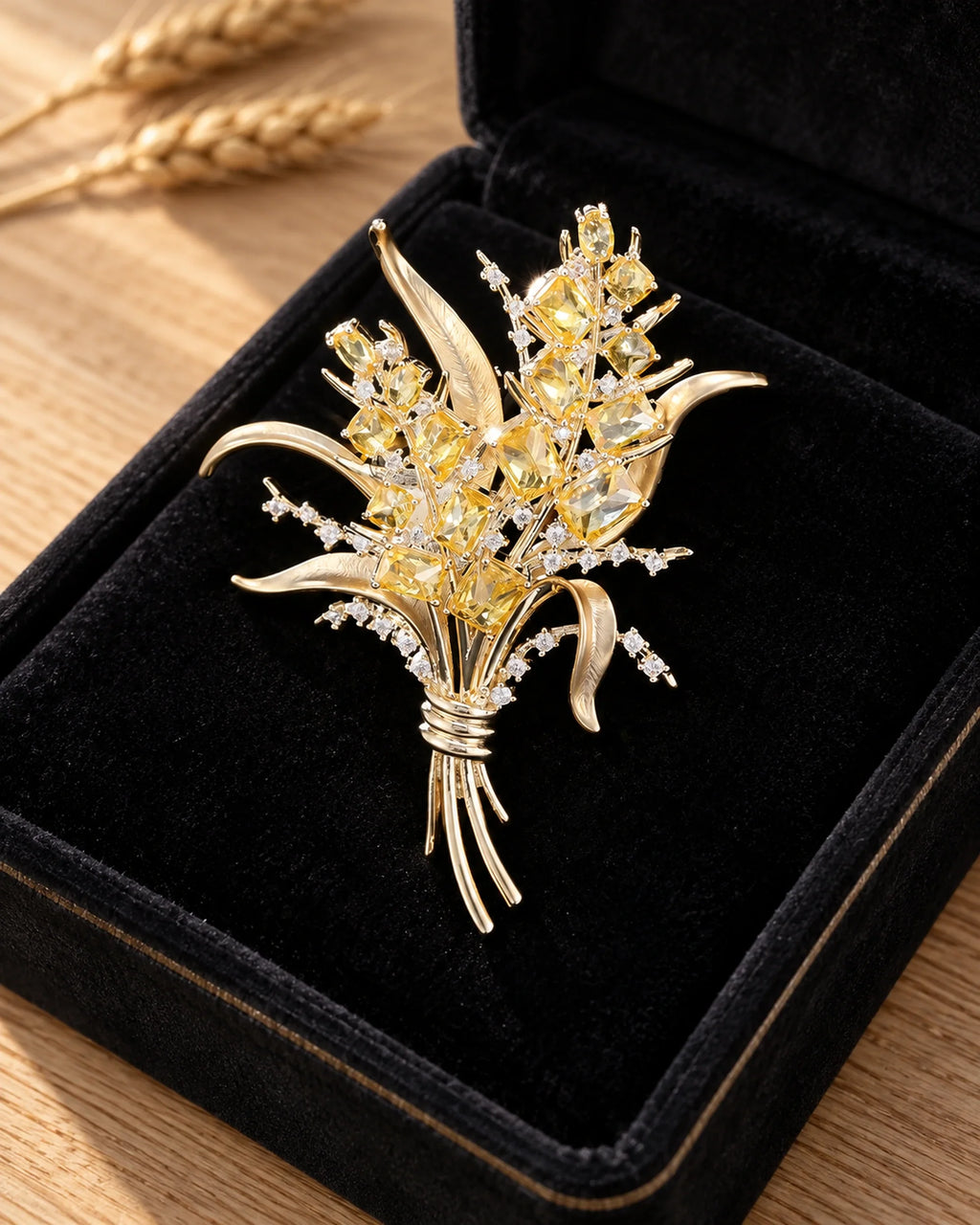 Aurea wheat sheaf brooch resting in a black velvet case with blurred wheat stalks behind, styling props shown
