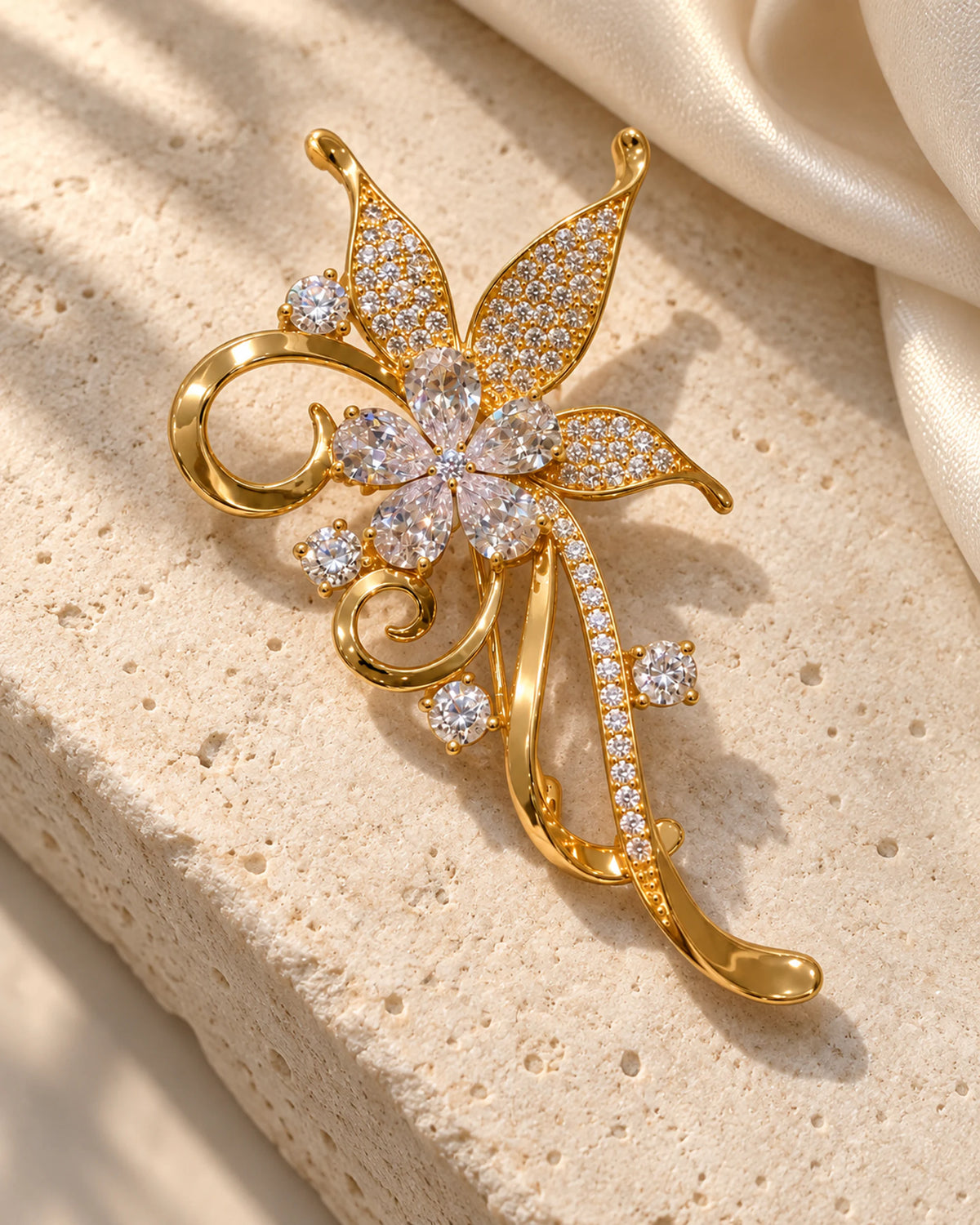 Avelia crystal scroll flower brooch on pale limestone beside ivory silk