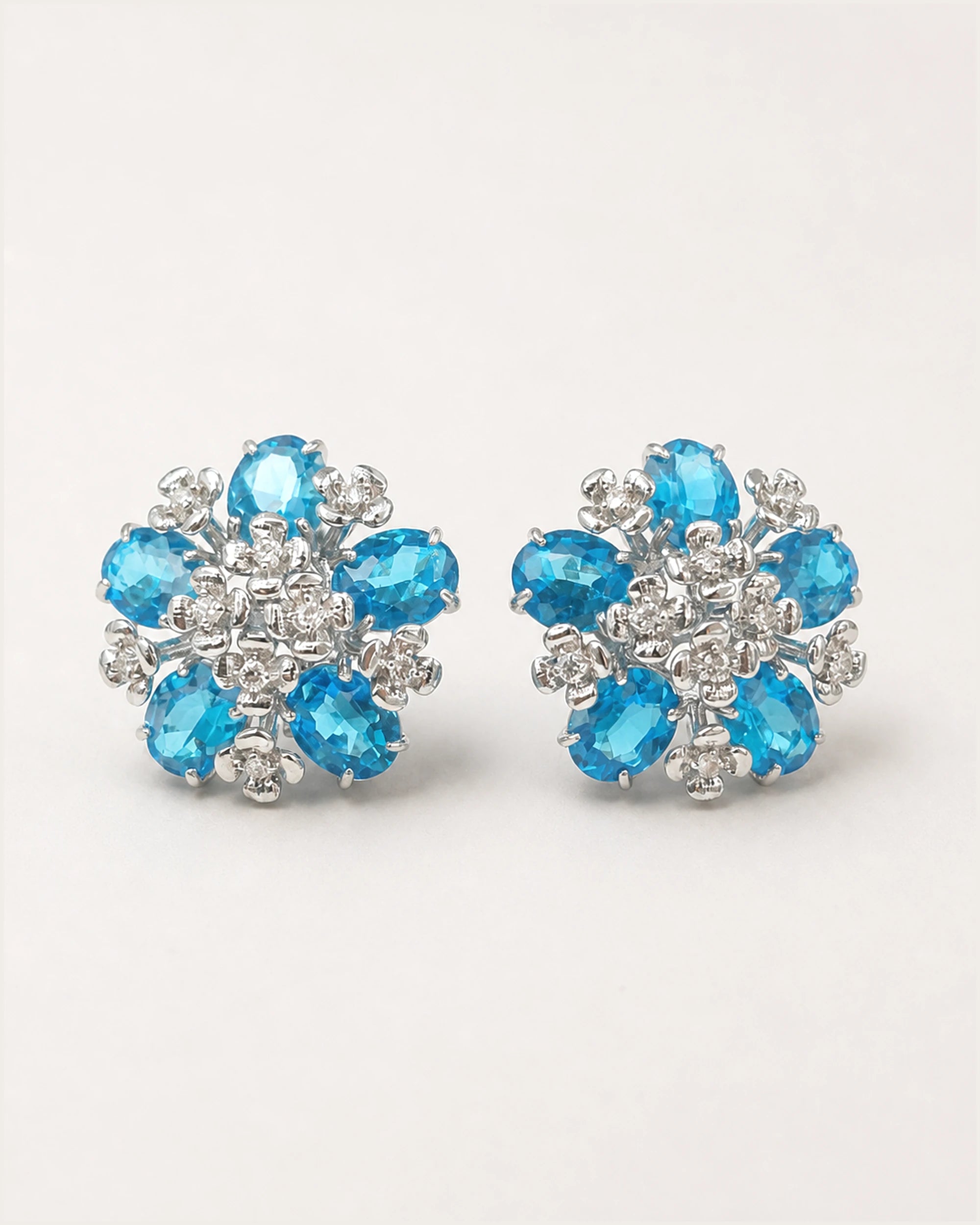 Azura Blue Glass Floral Omega-Back Earrings on an exact #F0EBE9 studio background with natural contact shadows.
