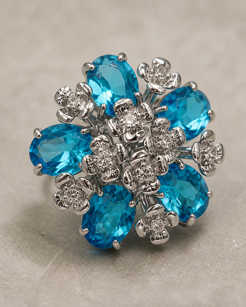 Macro view of the Azura earring's five aqua-blue faceted glass stones and silver-tone floral setting.