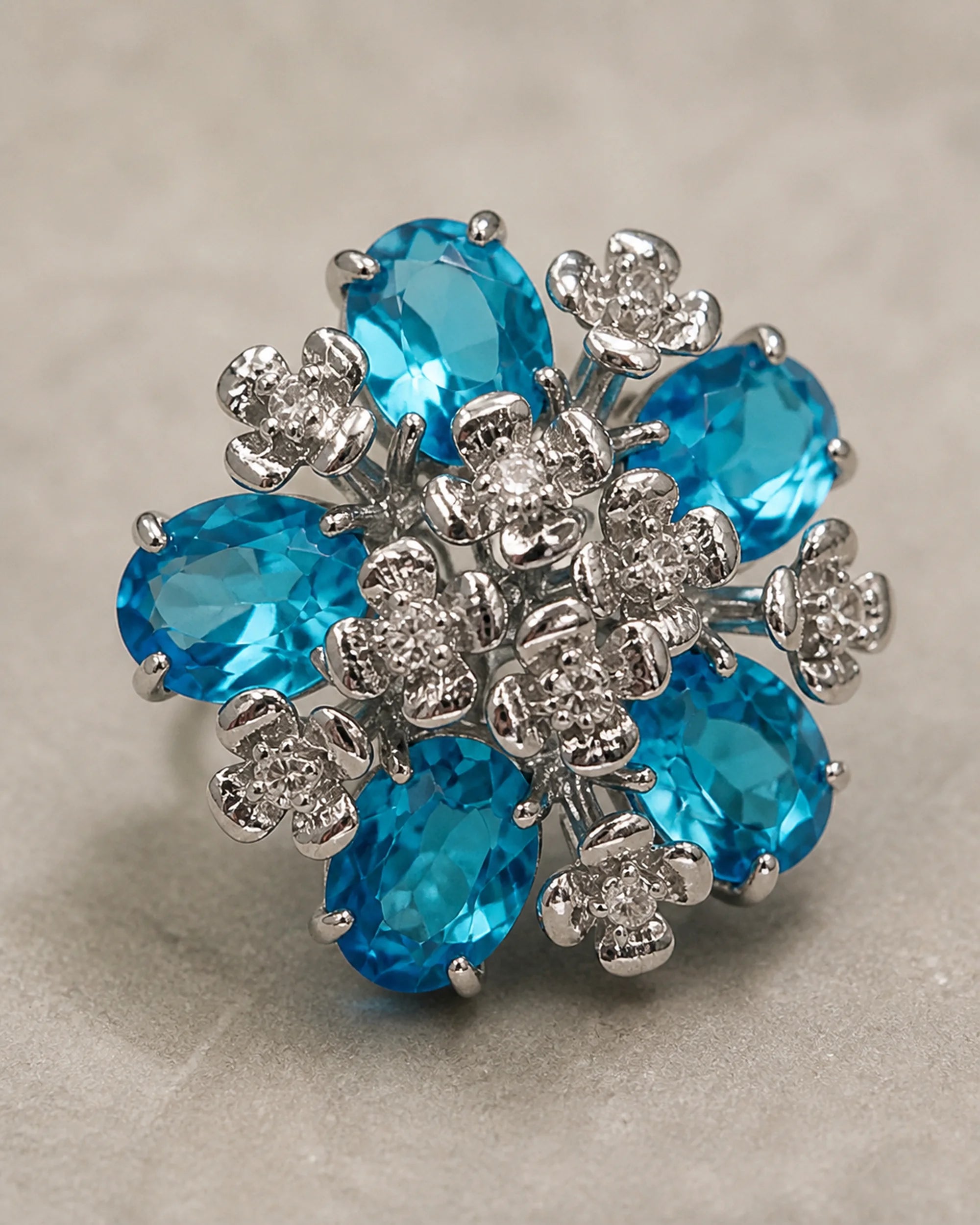 Macro view of the Azura earring's five aqua-blue faceted glass stones and silver-tone floral setting.