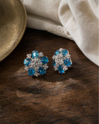 Azura silver-tone floral earrings resting in a realistic jewelry still life with aqua-blue glass stones visible.