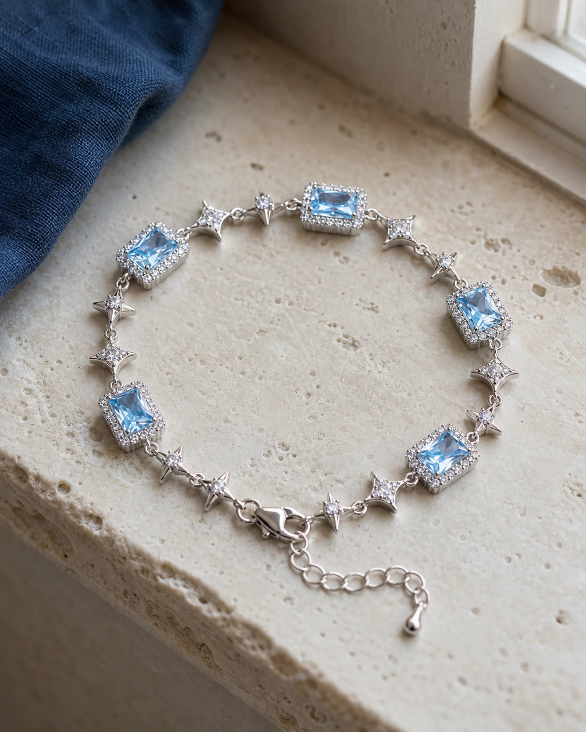 Celeste blue zircon star bracelet resting in a realistic stone-and-linen still life.