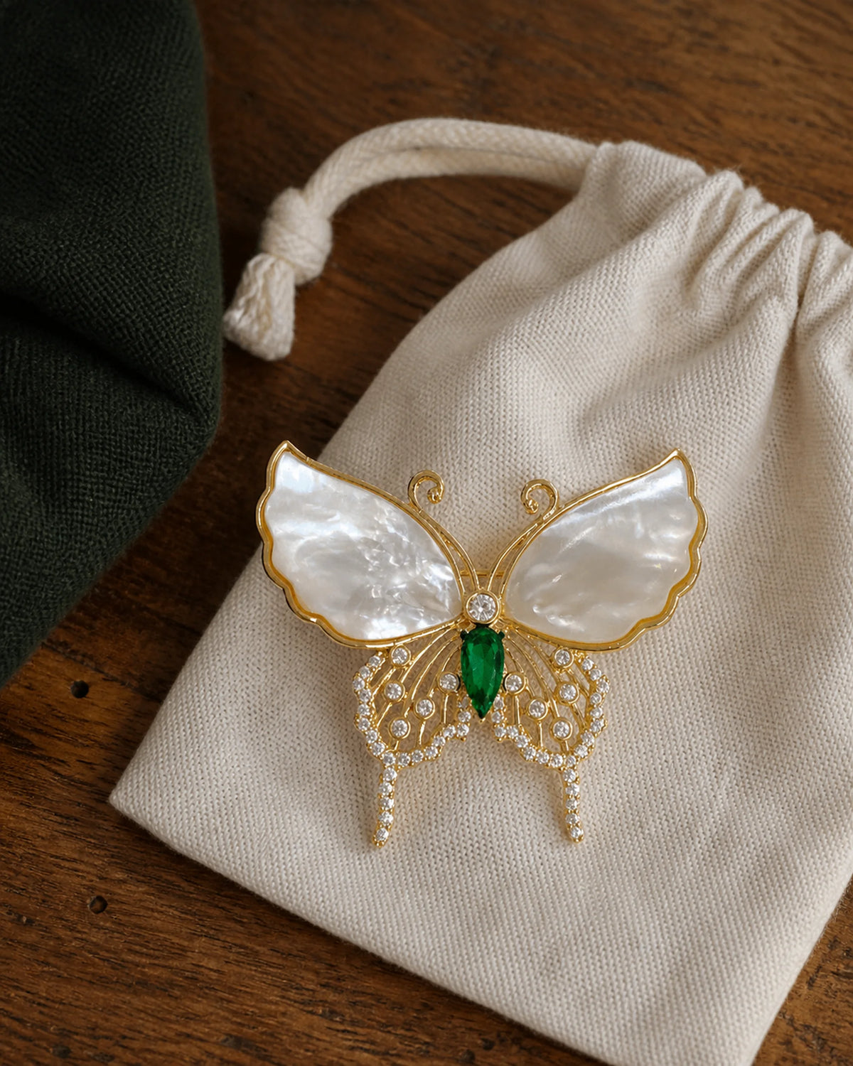 Elina gold-plated butterfly brooch resting on a linen jewelry pouch with its shell wings and green centre visible.