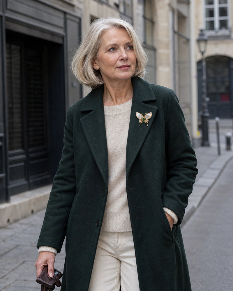 Elina green shell butterfly brooch worn on a deep green tailored coat in a wider city portrait.