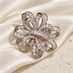 Silver-tone Elva ribbon rosette brooch resting on ivory silk over pale limestone