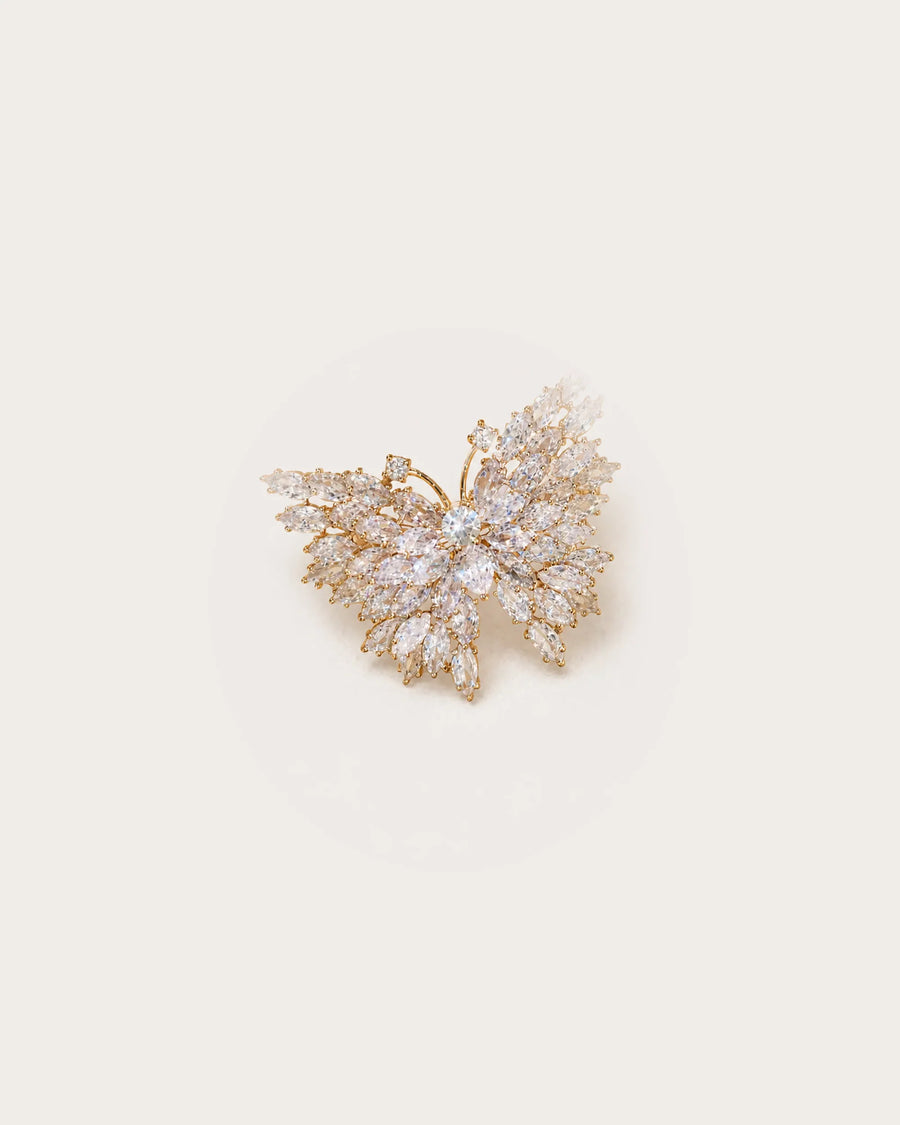 Eveli Marquise Crystal Butterfly Brooch on a warm #F0EBE9 studio background with a natural contact shadow