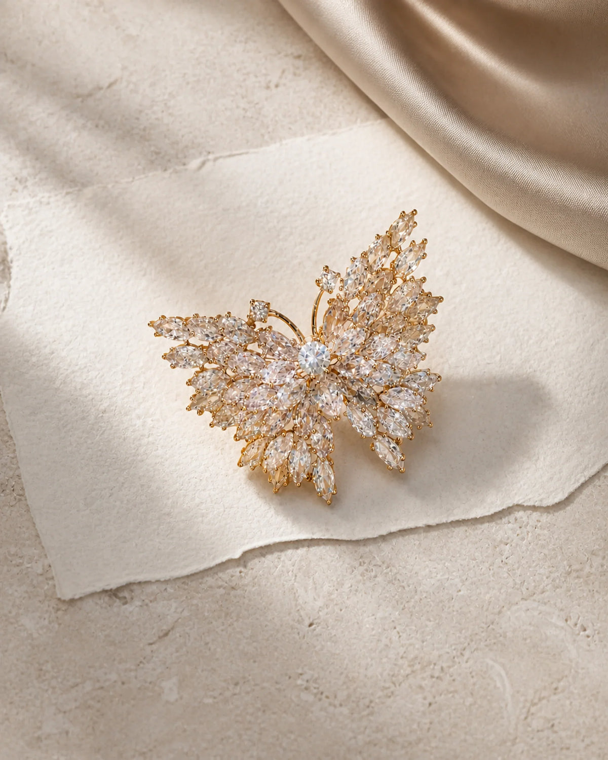 Eveli Butterfly Brooch resting on ivory paper, pale limestone and champagne silk in an original TUUGLOW still life