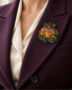 The Ornate Pumpkin sits within a deep aubergine lapel over a cream blouse.