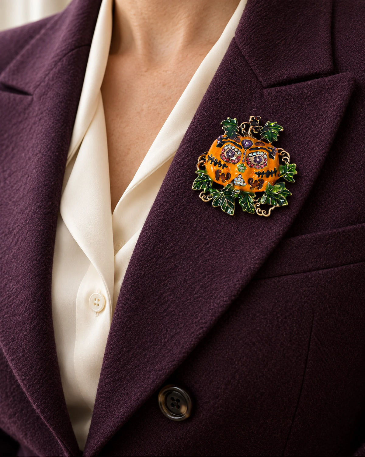 The Ornate Pumpkin sits within a deep aubergine lapel over a cream blouse.
