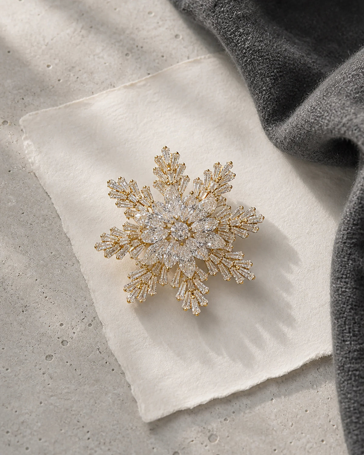 Halla Snowflake Brooch resting on ivory paper, pale limestone and charcoal wool in an original TUUGLOW still life