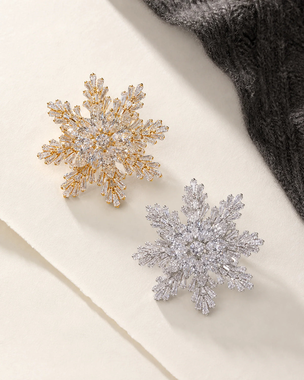Gold-tone and silver-tone Halla Eight-Point Crystal Snowflake Brooch variants on ivory paper