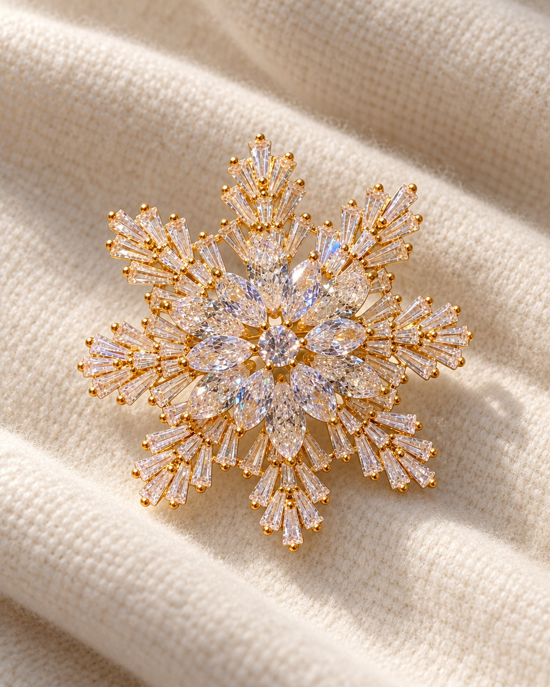 Halla crystal snowflake brooch, gold tone — three-quarter view on cream textile