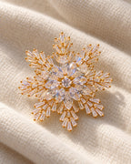 Halla crystal snowflake brooch, gold tone — three-quarter view on cream textile