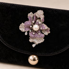 Iiris iris brooch secured to the reinforced velvet flap of a black evening clutch.