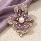 Complete Iiris iris brooch resting on pale limestone beside dusty-violet silk.