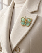 Ilma blue-green enamel butterfly brooch pinned within an ivory wool coat lapel.