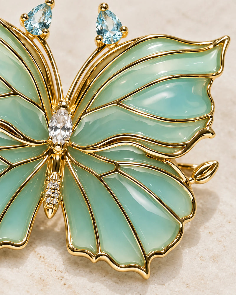 Detail of Ilma's translucent blue-green enamel wings, gold-tone veins and clear central stone.