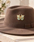 Ilma blue-green enamel butterfly brooch pinned directly to the wool crown of a taupe felt hat.