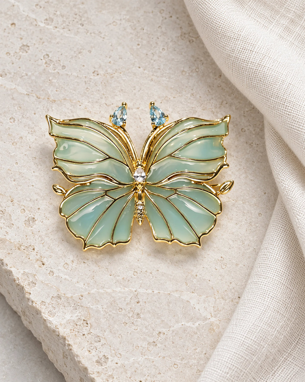 Ilma blue-green enamel butterfly brooch on limestone beside ivory linen
