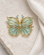 Ilma blue-green enamel butterfly brooch on limestone beside ivory linen