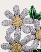 Detail close-up of Ilona zircon-set daisy petals, a gold-tone center and glossy green leaves