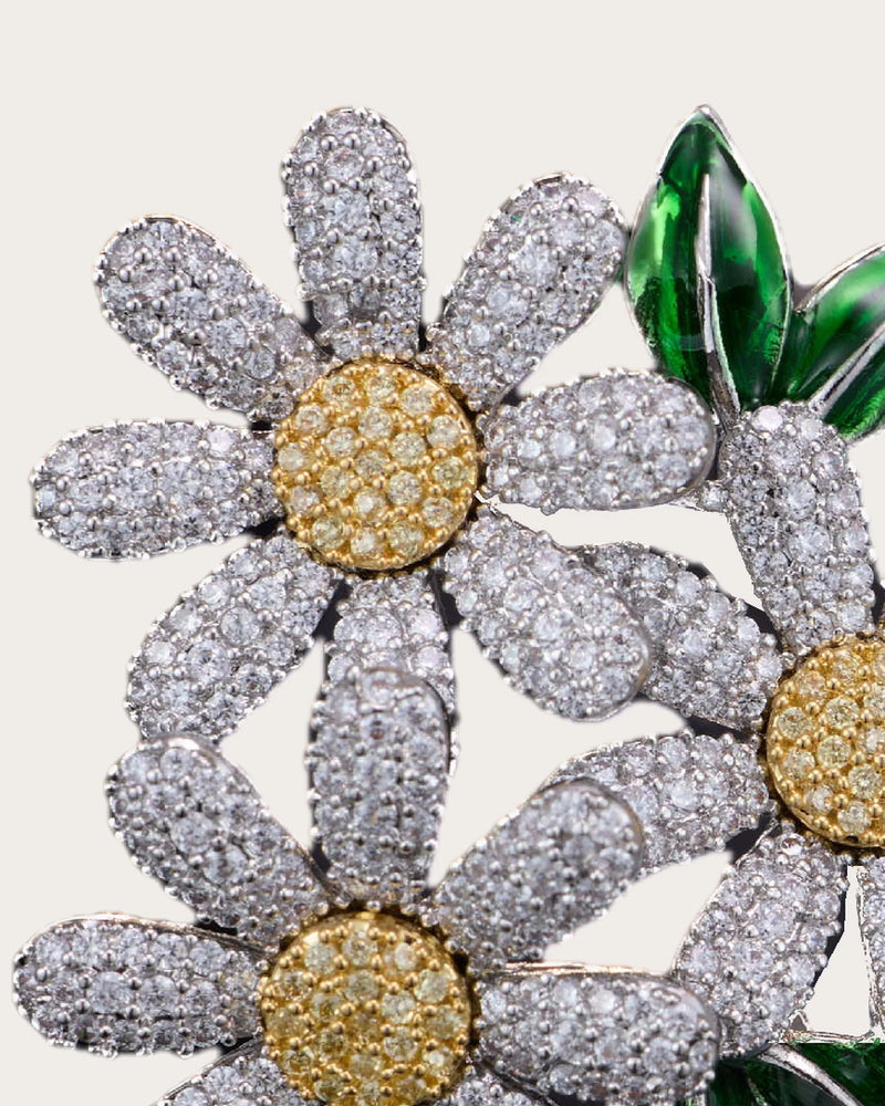 Detail close-up of Ilona zircon-set daisy petals, a gold-tone center and glossy green leaves