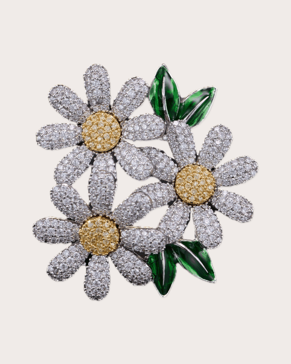 Ilona silver-tone daisy trio brooch with gold-tone centers and green leaves on a warm neutral background