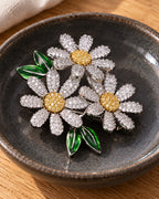 Ilona silver-tone daisy trio brooch resting in a dark ceramic dish on oak