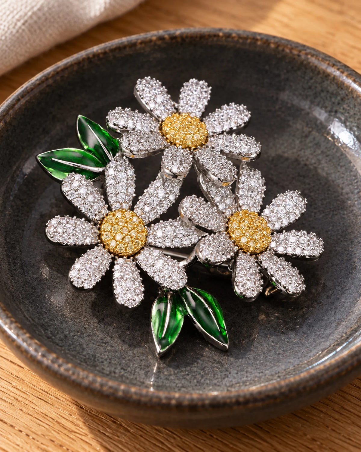Ilona silver-tone daisy trio brooch resting in a dark ceramic dish on oak