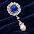 Inari blue cabochon and pearl-drop brooch displayed diagonally on midnight navy velvet.