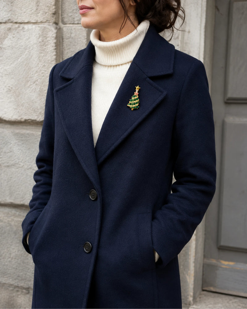 Green tree brooch worn on a navy wool coat above an ivory rollneck.