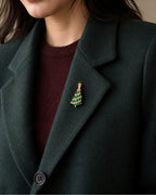 Small green Christmas tree brooch pinned inside a forest-green wool blazer lapel.