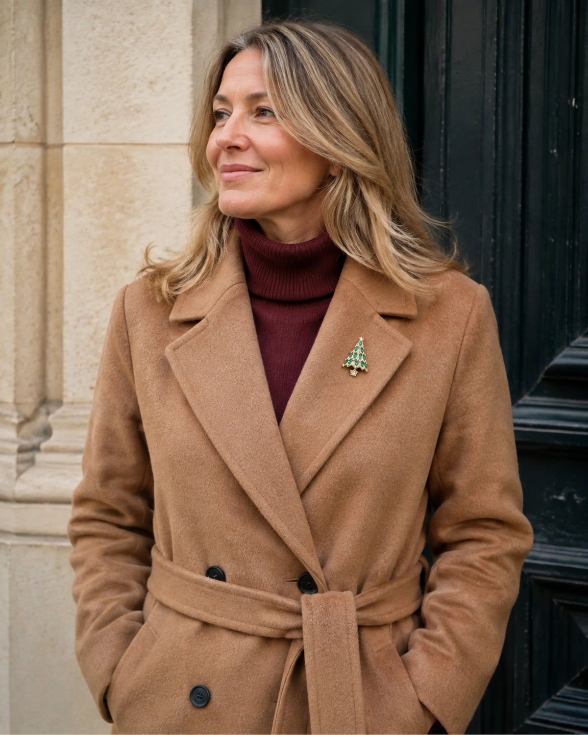 Wider wearing view of the Green Kuusi brooch on a camel coat and burgundy knit.