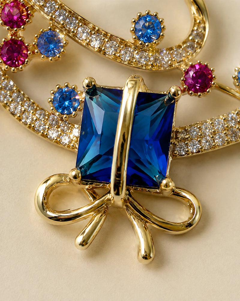 Macro view of the blue rectangular stone, gold-tone crossing band, open bow and crystal-set ribbon.