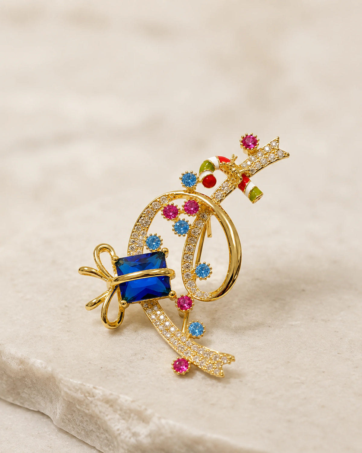 Angled display showing the open gold-tone curl, raised blue gift stone and striped candy-cane detail.