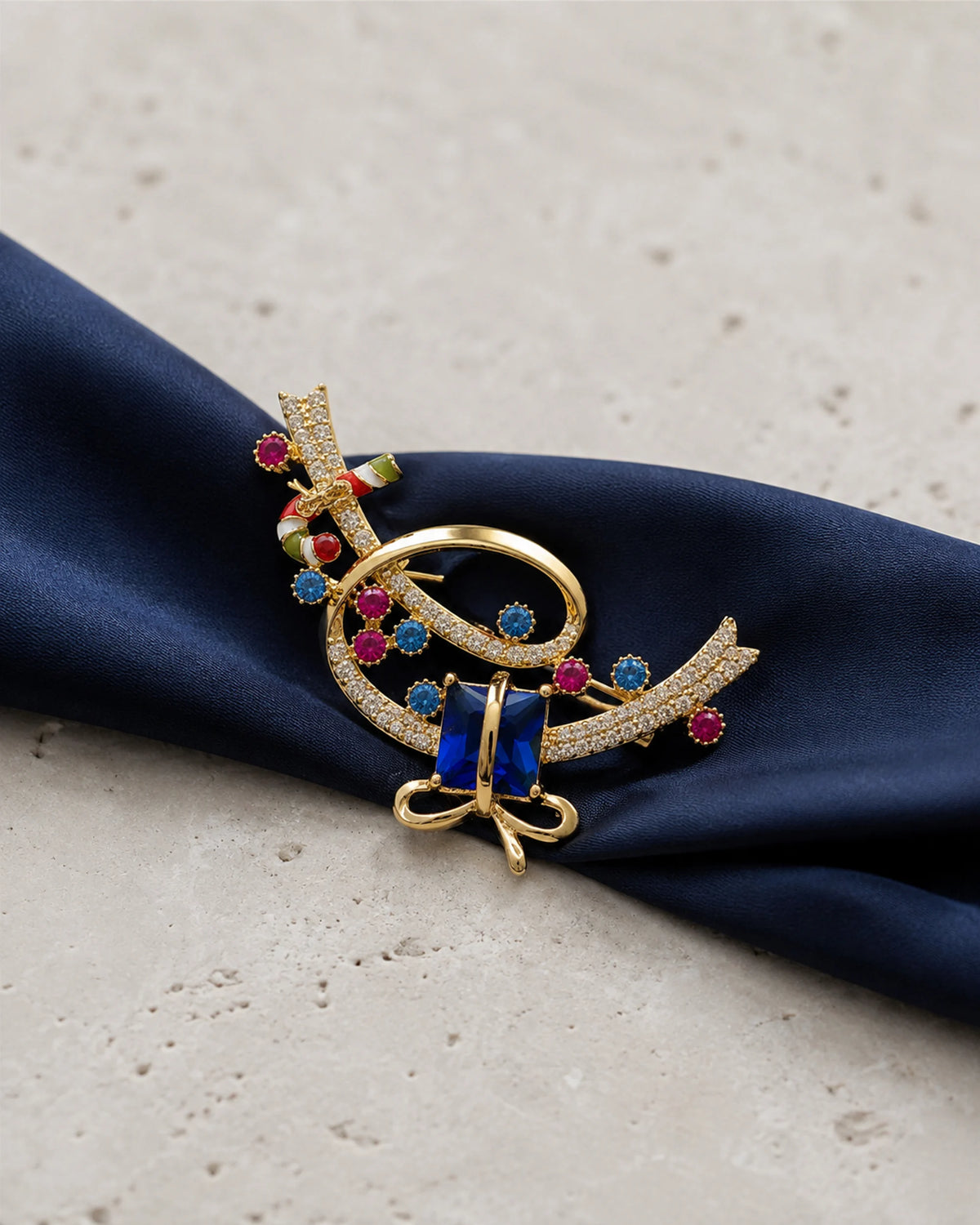 Complete Lahja brooch resting on navy ribbon over pale limestone.