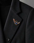 Close view of the small blue gift ribbon brooch pinned within a charcoal blazer lapel.