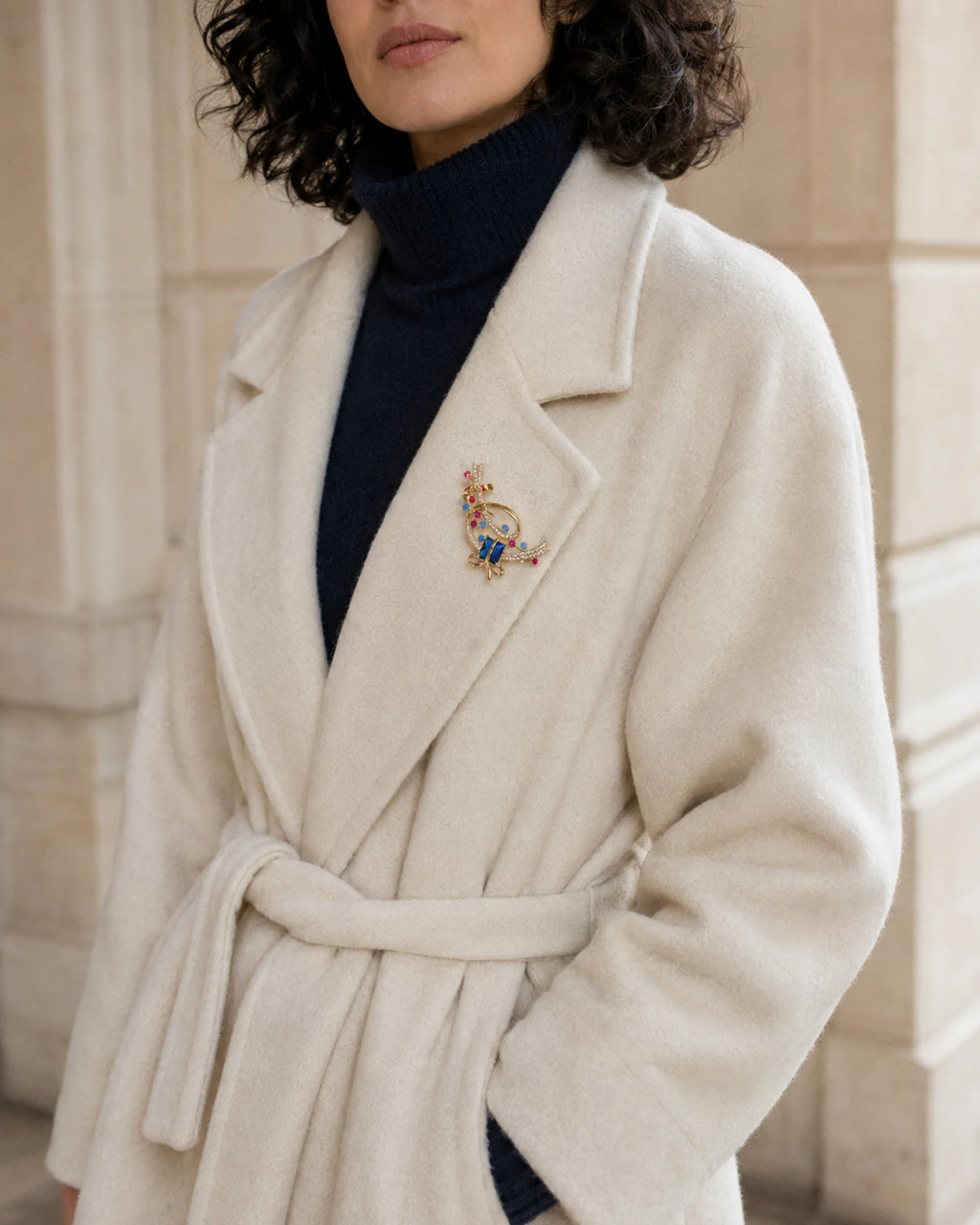 Wider view of Lahja worn on an ivory coat lapel over a navy knit.